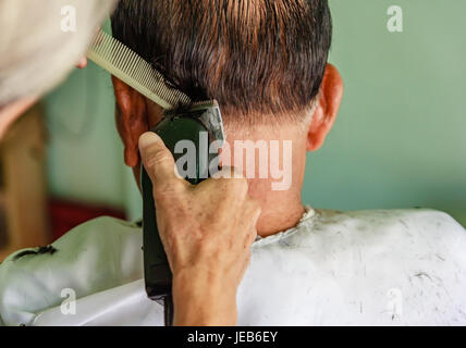 Master taglia i capelli e la barba di uomini del barbiere, parrucchiere rende l'acconciatura per un anziano uomo asiatico Foto Stock