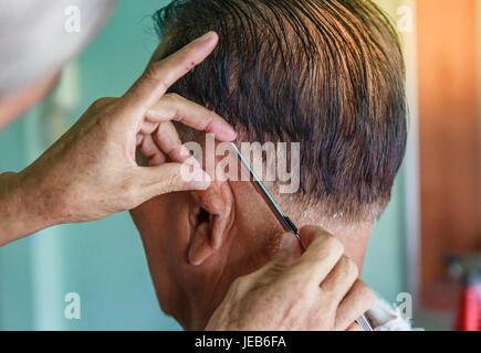 Master taglia i capelli e la barba di uomini del barbiere, parrucchiere rende l'acconciatura per un anziano uomo asiatico Foto Stock