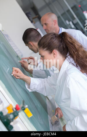 Ai giovani studenti la scrittura dei numeri sul verde chalk board in aula Foto Stock