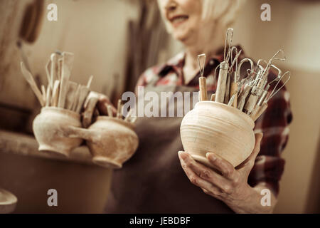 Senior donna tenendo ciotole con strumenti in ceramica a un workshop Foto Stock
