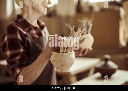 Senior donna tenendo ciotole con strumenti in ceramica a un workshop Foto Stock