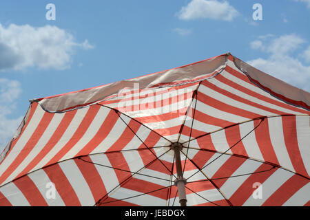 Red striped ombrello parasole per fornire ombra e la protezione solare contro il cielo blu con nuvole di luce Foto Stock