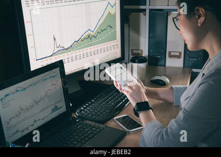 Ritratto di giovane imprenditrice asiatici utilizzando la calcolatrice per contare il nuovo tasso di cambio. seriamente ragazza concentrarsi sul trading currency. Foto Stock