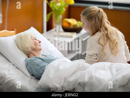 Vista laterale della ragazza visitando malati nonna giacente in letto di ospedale Foto Stock