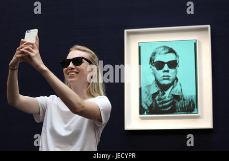Un visitatore prende un selfie con 'Self-Portrait' di Andy Warhol (prezzo stimato £5 milioni - £7 milioni) una delle opere in vendita al Sotheby's Contempory Art Evening sale il 28 giugno a Londra. Foto Stock
