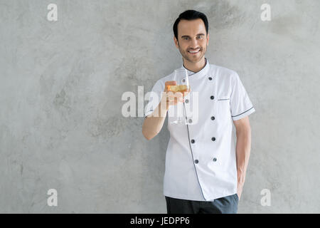 Ritratto di uomo caucasico cuocere tenendo un bicchiere di vino bianco. Girato nel ristorante. Foto Stock