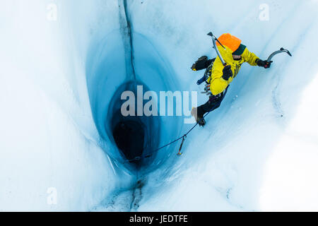 Un uomo che conduce una salita di ghiaccio al di fuori di un grande moulin o buco nel ghiaccio del ghiacciaio Matanuska in Alaska. Per iniziare la salita, lui e la sua belayer rappell Foto Stock