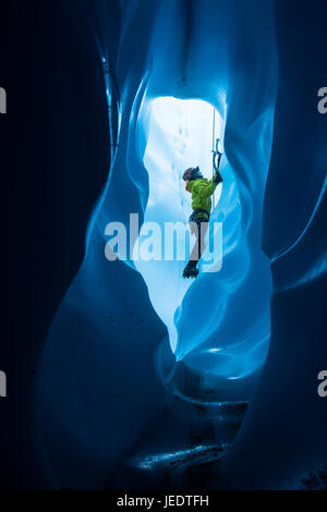 Un alpinista all interno di un grande tunnel di ghiaccio nel fondo di un moulin. Egli è la scalata verso l'ingresso superiore al foro Foto Stock