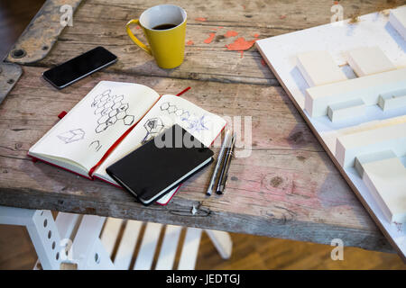 Notebook, Smartphone, modello architettonico e la tazza di caffè in un moderno ufficio informale Foto Stock