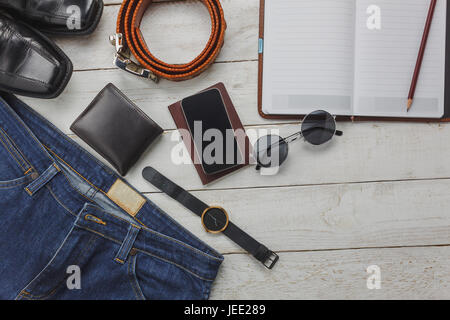 Vista superiore accessori per viaggiare con abbigliamento uomo concetto. shirt,jean,telefono cellulare su sfondo di legno.watch, occhiali da sole e scarpe sulla tavola di legno. Foto Stock