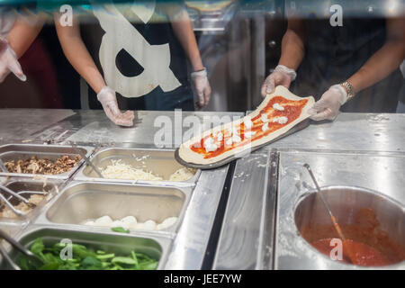 I dipendenti costruire una pizza a destra prima dei clienti' agli occhi in linea di assemblaggio di moda il giorno di apertura del &pizza nel loro primo New York pizzeria Martedì, 20 giugno 2017. &Pizza costruisce la sua pizze in un stile Chipotle modo con condimenti mettere sulla ristorazione per i clienti le preferenze individuali. Il 22 catena di negozi, soprattutto nell'area di Washington DC, bollette stesso in corrispondenza di un anti-stabilimento ristorante con forma oblunga pasticci creativi, alcuni ingredienti prodotti localmente e un hipster vibe con '&' tatuato dipendenti denominata "tribù". (© Richard B. Levine) Foto Stock