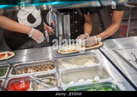 I dipendenti costruire una pizza a destra prima dei clienti' agli occhi in linea di assemblaggio di moda il giorno di apertura del &pizza nel loro primo New York pizzeria Martedì, 20 giugno 2017. &Pizza costruisce la sua pizze in un stile Chipotle modo con condimenti mettere sulla ristorazione per i clienti le preferenze individuali. Il 22 catena di negozi, soprattutto nell'area di Washington DC, bollette stesso in corrispondenza di un anti-stabilimento ristorante con forma oblunga pasticci creativi, alcuni ingredienti prodotti localmente e un hipster vibe con '&' tatuato dipendenti denominata "tribù". (© Richard B. Levine) Foto Stock