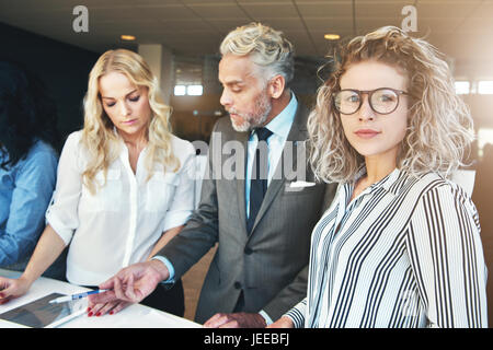 Giovane imprenditrice guardando la fotocamera mentre i colleghi lavorano con documenti in ufficio. Foto Stock