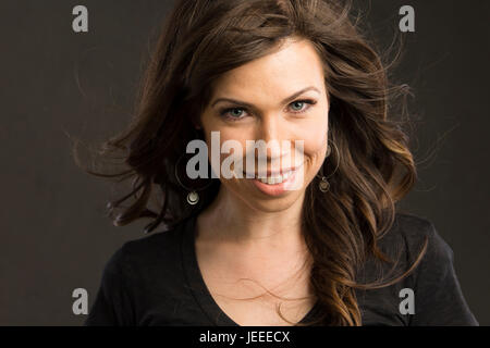 Giovane donna caucasica con capelli castani e un top nero sorrisi a viewer Foto Stock