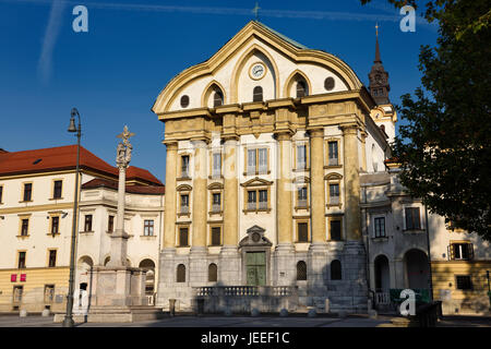 Sole sulla Chiesa delle Ursuline della Santissima Trinità con statue in marmo della colonna della Santa Trinità di Lubiana in Slovenia con orologio e la torre campanaria Foto Stock