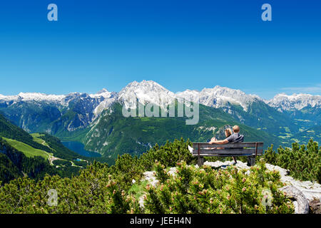 Coppia seduta su una panchina di fronte alle Alpi godendosi il panorama di montagna Foto Stock