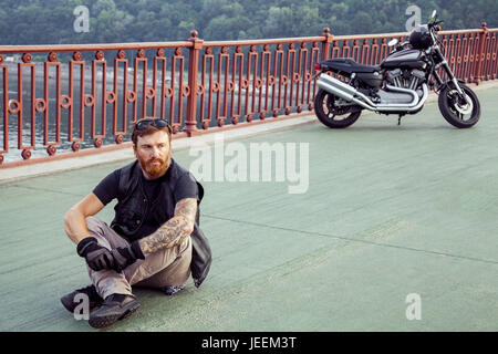 Barbuto redhead biker con la barba in giacca di pelle seduta sul pavimento. Foto Stock