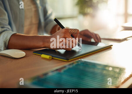 Primo piano della donna di mano utilizzando una tavoletta grafica e penna stilo. Femmina di designer che lavora alla sua scrivania Foto Stock