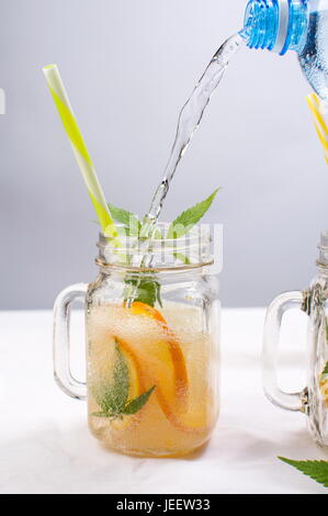 Versare acqua nel vaso con arancia e foglie di menta Foto Stock