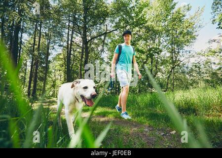 Giovane uomo che cammina con il suo cane (labrador retriever) nella foresta. Orario estivo e vacanze in tema. Foto Stock
