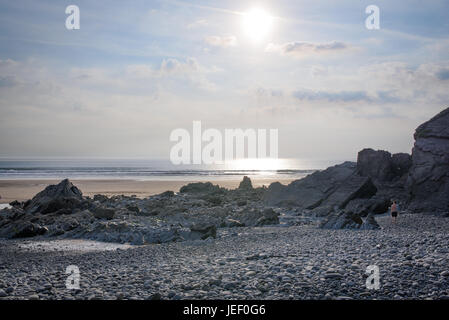 Il sole nel cielo e riflettendo sulle onde a Sandymouth Beach Foto Stock