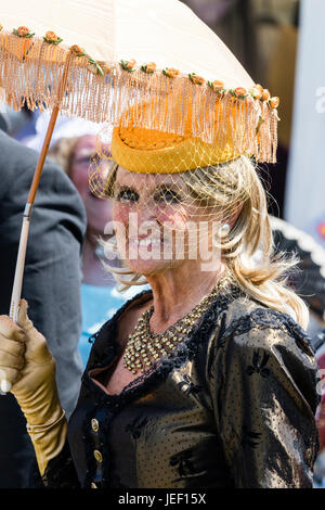 Ritratto, all'aperto, di alti donna, 60s, vestito in costume Vittoriano. Azienda parasol, indossa il cappello con velo, sorridente. Foto Stock