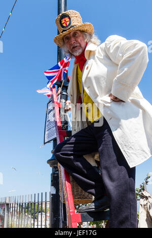 Signor William Thompkins, Lamplighter, Charles Dickens carattere, storia. Indossare camice bianco e cappello di paglia, sorge su scala contro luce con Union Jack. Foto Stock