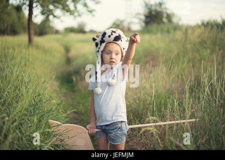 Kid in animali divertenti hat giocando con il giocattolo di legno sul cavallo tramonto Foto Stock