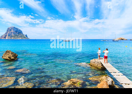 Isola di Ibiza, Spagna - 18 Maggio 2017: l uomo sta immagine di donna in piedi sul piccolo molo di legno in Cala d'Hort bay e vista di Es Vedra island, Ibiza ho Foto Stock