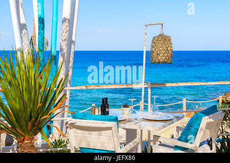 White tavolo e sedie con cuscini blu sulla terrazza ristorante sulla spiaggia di Cala Nova con bellissima vista sul mare e isola di Ibiza, Spagna Foto Stock