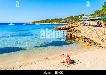 CALA PORTINATX, isola di Ibiza - Maggio 22, 2017: donna seduta sulla spiaggia e la lettura di libro in Cala Portinatx bay sull isola di Ibiza, Spagna. Foto Stock