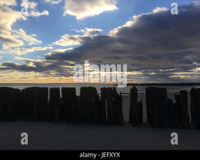 Fila di tralicci in legno da andato lungo molo sulla spiaggia di Coney Island, Brooklyn, New York. Tramonto spettacolare sulla spiaggia, puffy nuvole. Foto Stock