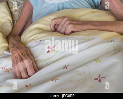 Braccia scarne e le mani di un molto vecchia donna giacente in un letto Foto Stock