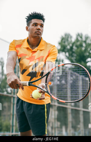 Basso angolo di vista determinata giovane uomo nero gioca a tennis Foto Stock