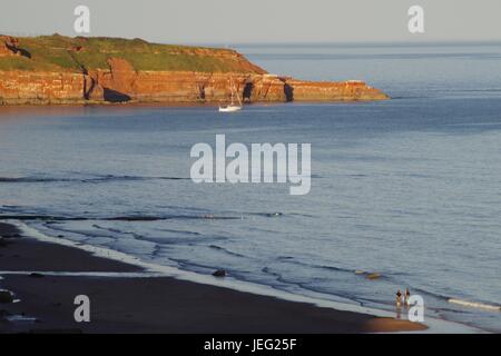 Uno yacht ormeggiato dalla scogliera di arenaria rossa di Straight Point a Sandy Bay. Devon, Regno Unito. Giugno 2017. Foto Stock