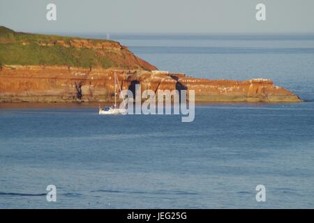 Uno yacht ormeggiato dalla scogliera di arenaria rossa di Straight Point a Sandy Bay. Devon, Regno Unito. Giugno 2017. Foto Stock