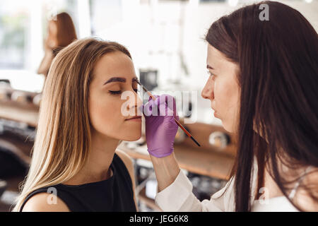 Ritratto di professional cosmetologo in viola guanti rendendo sopracciglia permanente Foto Stock