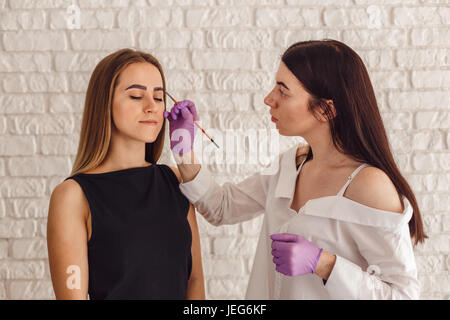 Master cosmetologo dipinta su sopracciglia femminile nel salone di bellezza Foto Stock