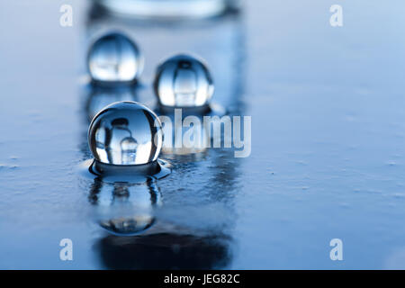 Perle di acqua abstract con bottiglia di vetro e la riflessione sulla superficie scura. Foto Stock