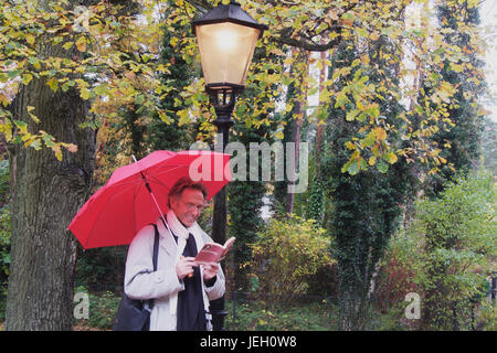Mann, mittleren altera, mit Regenschirm bei Straßenlaterne, liest ein Buch | middleaged uomo con un ombrello accanto ad un lampione è la lettura di un libro Foto Stock