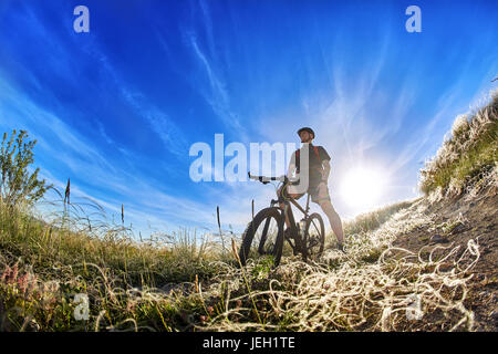 Basso angolo vista del ciclista in piedi con la mountain bike sul sentiero di sunrise. Foto Stock