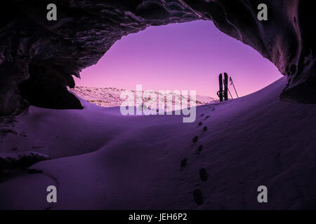 Footprints conducono verso un splitboard collocato all'entrata di una caverna di ghiaccio entro Canwell ghiacciaio in Alaska Range dopo il tramonto in inverno Foto Stock