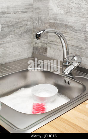 Chiusura del lavello pieno di schiuma, vasellame e rosa Spugna per pulizia Foto Stock