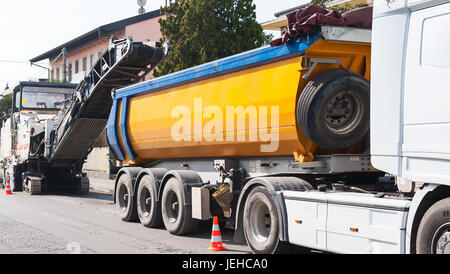 La costruzione di strade, asfaltatura di una strada. Dumper è caricato con asfalto fresato da pialla a freddo la macchina. Foto Stock