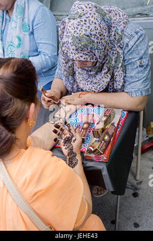 Un islamico donna in abiti tradizionali decora una donna di mano con henné per celebrare l'Eid Al Fitr segna la fine del Ramadan. Queens, NYC. Foto Stock