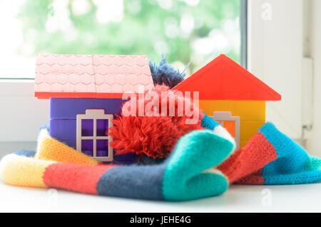 Casa giocattolo sul davanzale della finestra avvolto in una sciarpa. Il riscaldamento della casa. Foto Stock