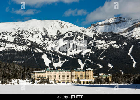 Lo Chateau Lake Louise in inverno con il lago congelato e coperta di neve e montagne sullo sfondo di nuvole e cielo blu Foto Stock