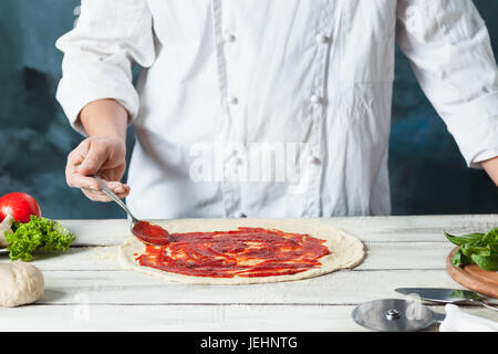 Closeup mano dello chef baker in bianco rendendo uniforme la pizza di cucina Foto Stock