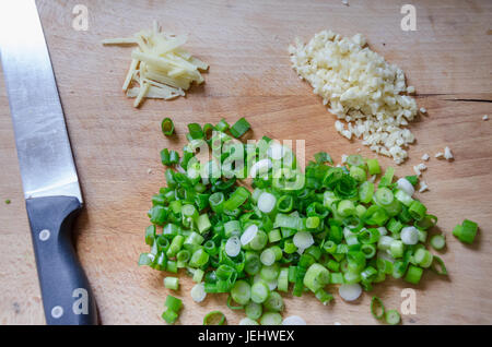 Molla tritate le cipolle, aglio e zenzero su un tagliere di legno con un coltello da cucina. Foto Stock
