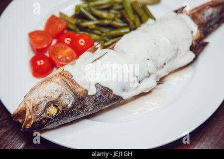 Branzino grigliato servito su una piastra con varie salse e verdure Foto Stock